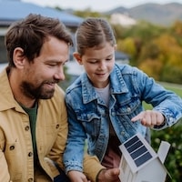 Little girl with her dad holding paper model of house with solar panels, explaining how it works